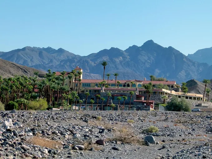 A palm-lined resort building in a rocky desert below mountains
